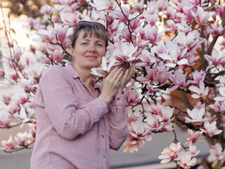 Woman gently touching blooming magnolia flowers (Magnolia) in spring garden, soft pink color palette, concept of spring blossom, enjoying nature and seasonal beauty. © Natallia