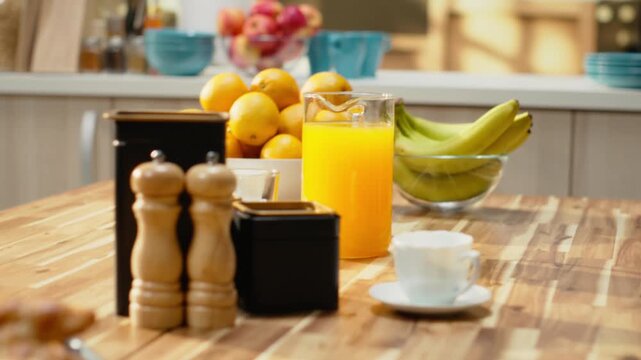 Kitchen with wooden breakfast table with pastry and fruits in empty home, natural light enhances rustic design, showing kitchenware and utensils. Decorative items in spacious room with no people.