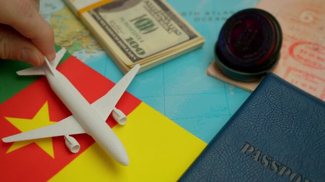 Global travel theme with airplane landing beside passport and money stack on Cameroon flag world map.