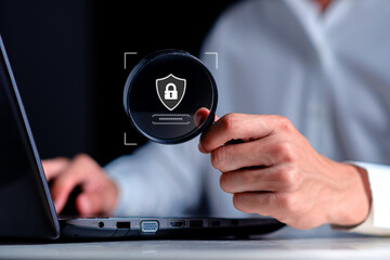Hand holding magnifying glass analyzing secure login interface with shield and lock icon on laptop screen, representing cybersecurity investigation, password protection, data privacy authentication