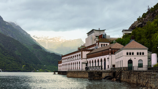 Tyssedal hydroelectric legacy as power station buildings standing above fjord water beneath steep mountains, reflecting Norway early hydropower development, infrastructure history concept