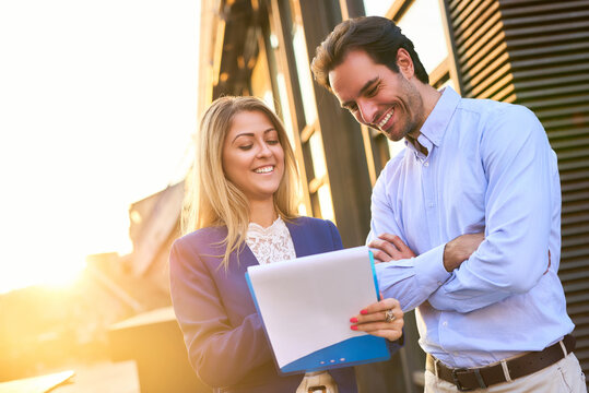 Business colleagues collaborating outdoors, discussing paperwork and smiling, enjoying successful teamwork and corporate partnership in natural light
