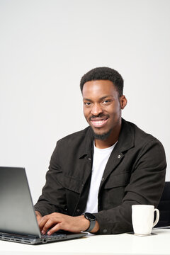 Young african american man working remotely on a laptop, smiling confidently and happily, embracing professional development and modern technology in a bright workplace