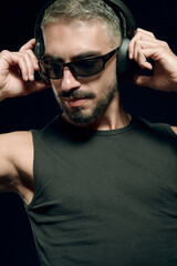 Obraz premium Stylish man with beard and sunglasses enjoying music, adjusting wireless headphones, listening to audio in a focused pose, embracing cool sound and personal hobby