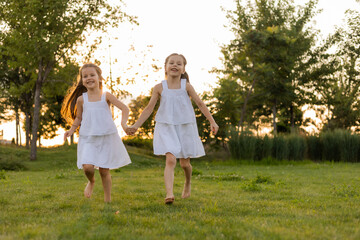 Obraz premium two little girls in white cotton dresses playing on a summer lawn at sunset