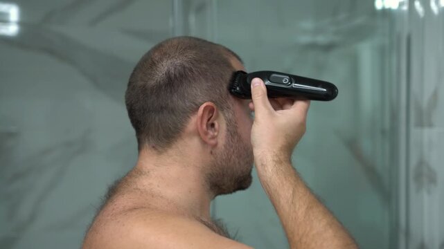 Man Cutting His Own Hair with Electric Hair Clipper in Bathroom