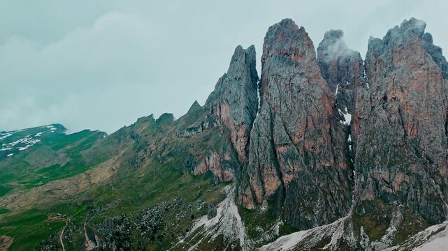 Seceda peak with alpine slopes and cloudy sky in Italian Dolomites, aerial drone view. Iconic jagged peak of Seceda in Dolomites