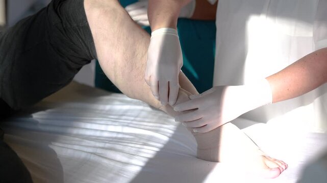 Nurse instructs student in compression bandaging technique on patient leg during clinical training session