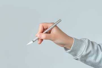 Hand holding an Exacto craft knife against a neutral background	