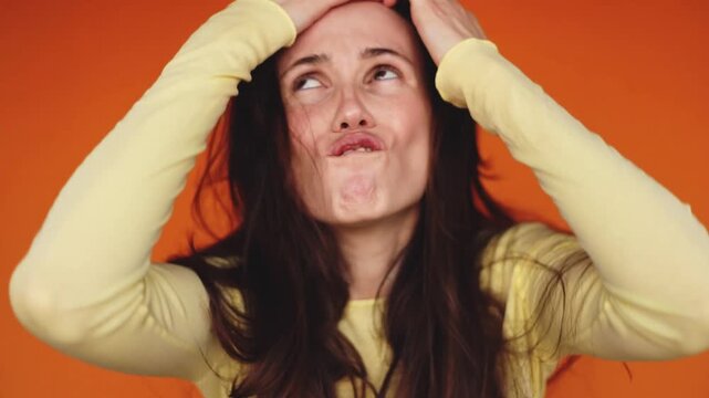 Horizontal video of angry woman shouting, rolling eyes and walking away on orange background. Furious brunette girl screaming, gesturing with hands and leaving the frame. Conflict and anger concept