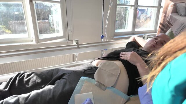 Clinical instructor teaching student nurse details of ostomy bag management during colostomy care with patient