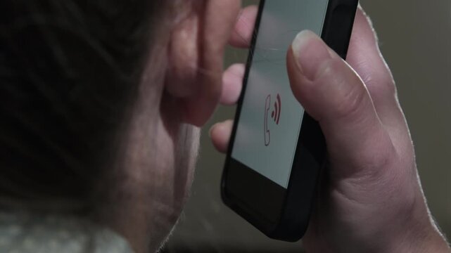Woman talking on mobile phone holding smartphone in hand near ear in dimly lit room close-up back view