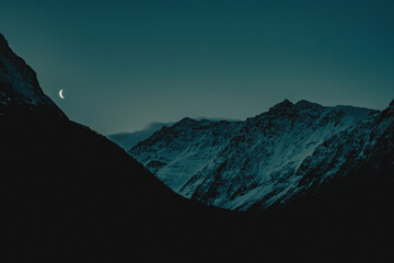 Waning crescent moon over dramatic snowy mountain range at blue hour twilight © megumy