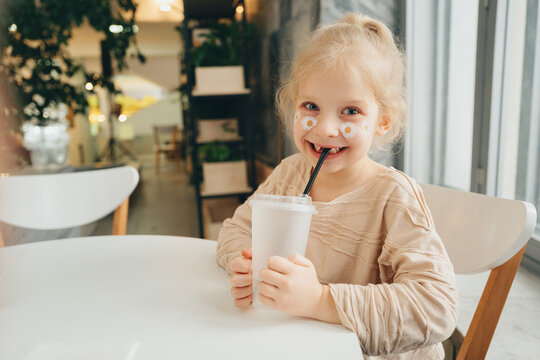 A child with a cocktail and a straw drinks from a disposable plastic container in a cafe during the day.