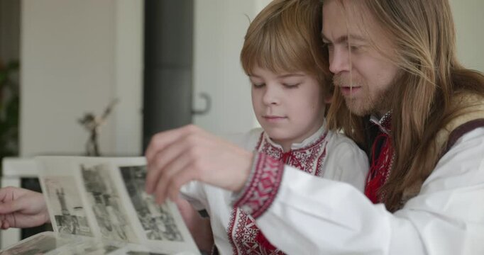 Man and Kid Boy Watch Family Album Together. Family in Ukrainian Traditional Attire Father Dad Son Relations Childhood. 4K 10-bit