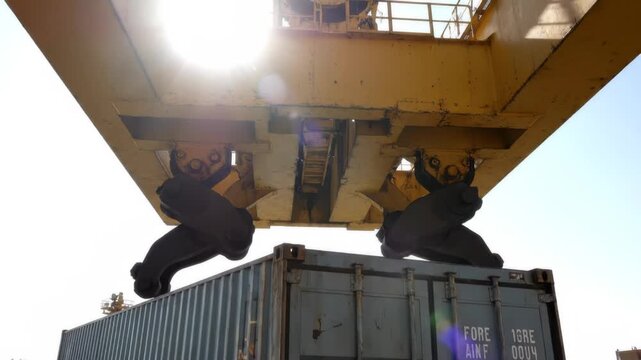 Low angle shot of industrial crane lowering spreader onto shipping container