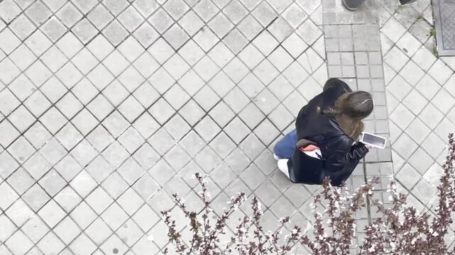 Joven con tel&eacute;fono m&oacute;vil andando por acera de calle desde arriba en perspectiva a&eacute;rea
