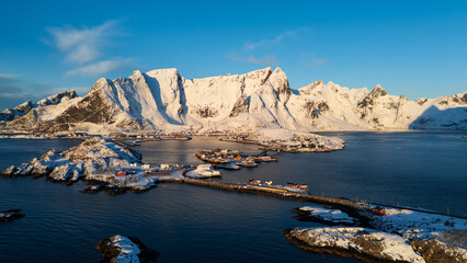Naklejka premium Aerial view of snow covered mountains and fishing village on a fjord in Lofoten, Norway
