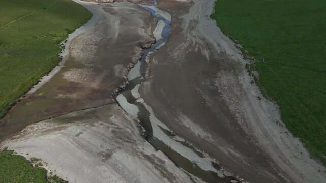 Aerial view of a dry riverbed with green banks and a narrow channel of water flowing through.