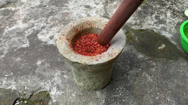 pounding dried chili pepper in a mortar. chili powder preserve food.