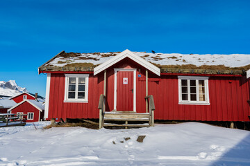 Traditional red wooden cabin with turf roof in snowy winter landscape under clear blue sky