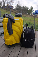 Fototapeta premium Yellow Suitcase Topped With Jacket And Vintage Camera On Wooden Deck, Creative Escape Mood For Photographer On Roadtrip, Layered Textures And Equipment Imply Storytelling And Exploration