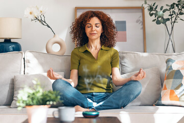 Relaxing mature woman doing yoga exercises on the couch at home