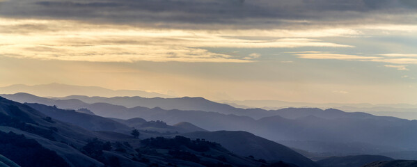 Naklejka premium Panorama from view of valley and mountains with layers at sunrise, sunset, with clouds in sky