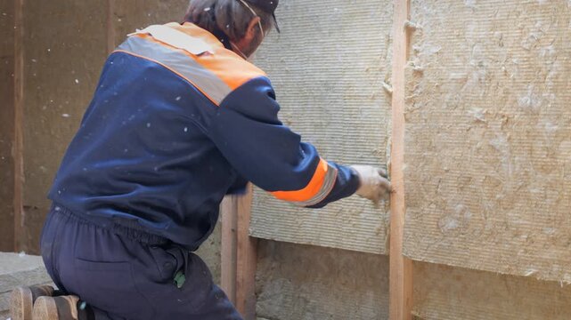 Insulation of a frame house with mineral wool. Cutting, fitting, laying insulation. Construction works.