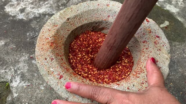 pounding dried chili pepper in a mortar. chili powder preserve food.
