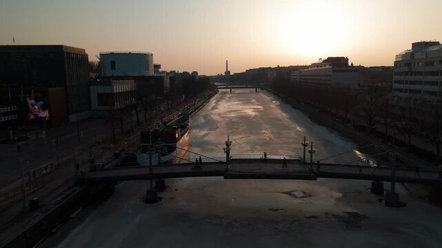 Aerial cinematic flight along the frozen Aura River (Aurajoki) at sunset, Turku, Finland.