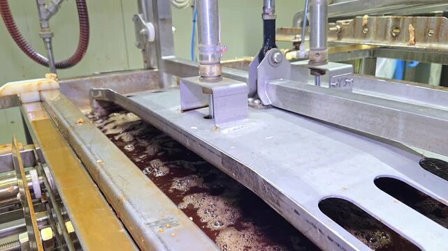 Automated industrial pusher machine soaking tofu blocks into brine on a conveyor belt.