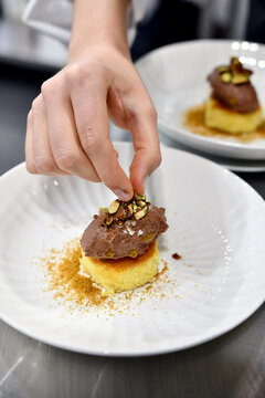 experto chef emplatando con sus manos un postre con ingredientes como helado de chocolate y pistacho con bizcocho