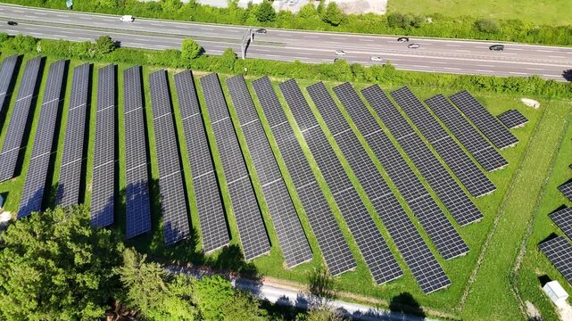 Aerial drone footage of orbiting over photovoltaic solar panels next to a highway in summer