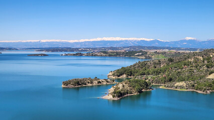 Fototapeta premium A breathtaking panoramic view of the Seyhan Dam Lake in early spring, featuring its signature turquoise waters reflecting the surrounding snowy hills under a crisp March sky, symbolizing the vibrant l