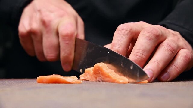 Chef slices fresh salmon fillet on wooden cutting board with sharp knife