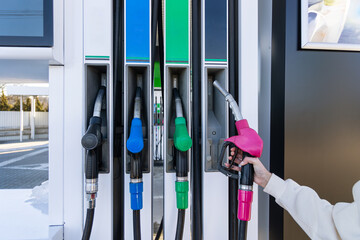Hand Holding Pink Fuel Nozzle at Pump. Person selecting a pink fuel nozzle at a gas station pump, with colorful handles showing refueling, transport, and everyday energy use. © Iryna