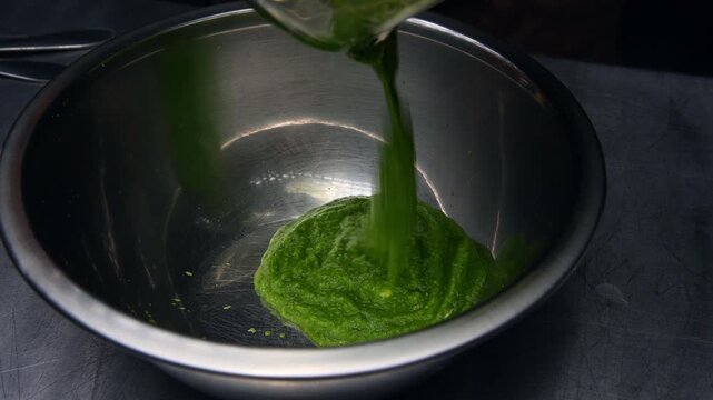 Green spinach puree being poured into a stainless steel mixing bowl