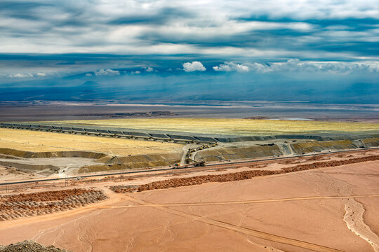 A wide aerial view shows multiple leach pads contained within berms and connected by long, portable conveyor belt systems in a desert mining operation in Chile