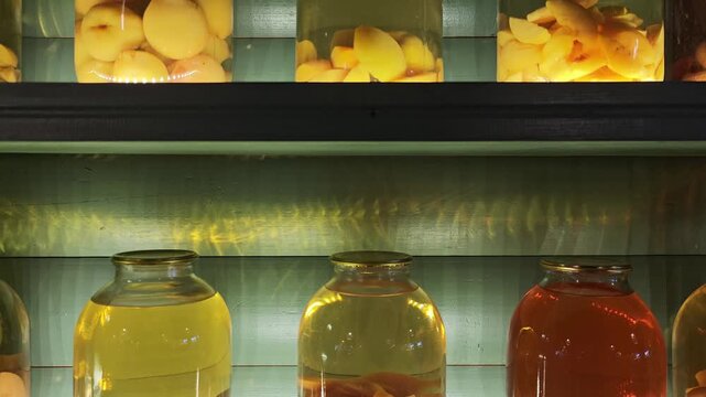 Rows of large glass jars filled with colorful homemade fruit compote and preserves. Traditional canning method for storing harvest