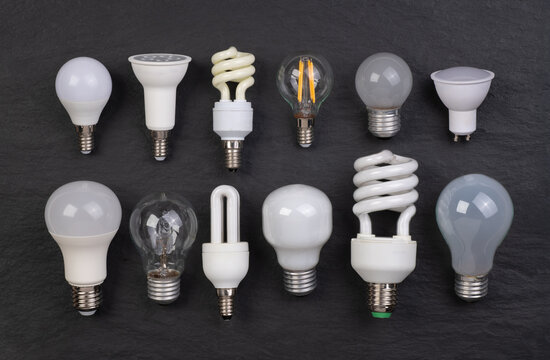 Assortment of different kinds of light bulbs on black background, top view