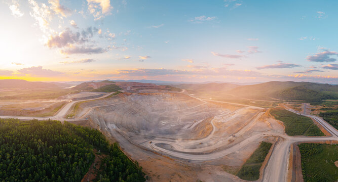 Panoramic view of industry landscape open pit mining at sunset with vast dirt roads and surrounding forest
