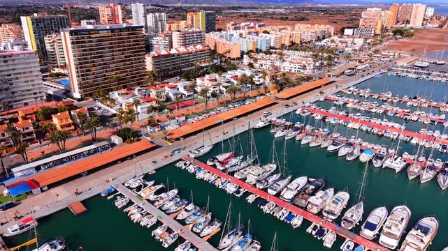 Rows of sailboats and motor yachts moored at a pier near city buildings. Aerial view of luxury yachts docked in a harbor.