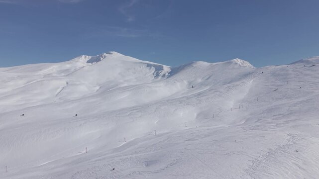 Aerial tilt up shot revealing the majestic snow-capped mountain peak of Uludag against a clear blue sky