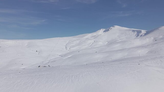 Aerial forward tracking shot flying towards the majestic snow-capped mountain peak of Uludag under a clear blue sky