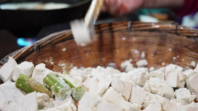 Fresh tofu cubes and green garlic segments placed in a woven bamboo basket for cooking preparation