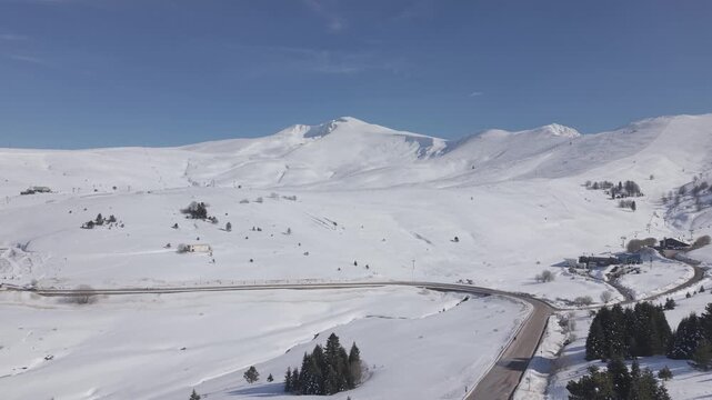 Aerial forward tracking shot over a snow-covered ski resort and mountain road at Uludag