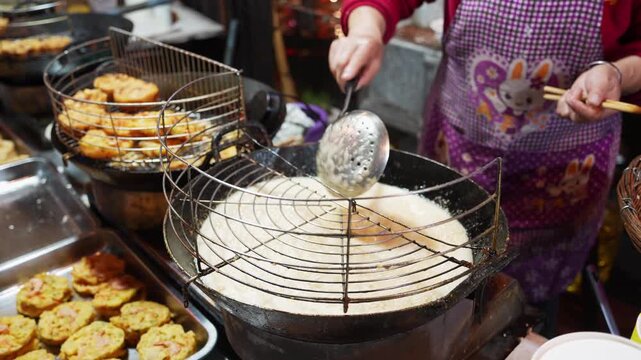 Street vendor frying traditional snacks at a night market using a large wok and wire strainer