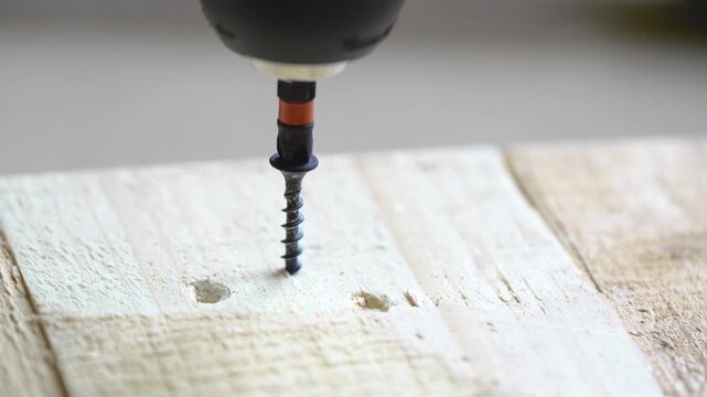 Electric screwdriver driving metal screw into wooden block with high-pitched squeaky sound
