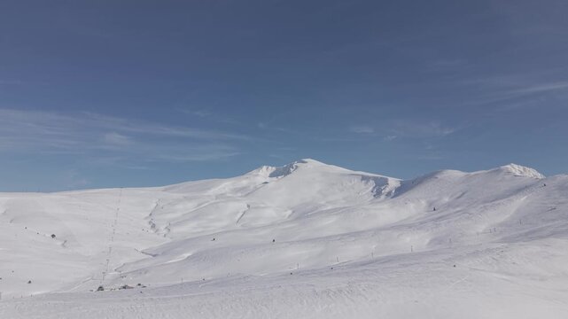 Aerial forward tracking shot flying towards the majestic snow-capped mountain peak of Uludag under a clear blue sky
